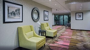 Eine Hotelhalle mit zwei gelben Sesseln, einem gemusterten Teppich, gerahmten Bildern an den Wänden und einem großen Spiegel.