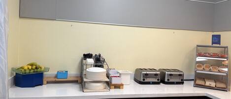 A breakfast bar with a fruit bowl, a dish rack, a toaster, and a bread display.