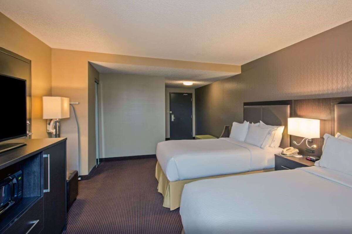 A hotel room with two beds, a TV, a desk with a lamp, and a door leading to another room.
