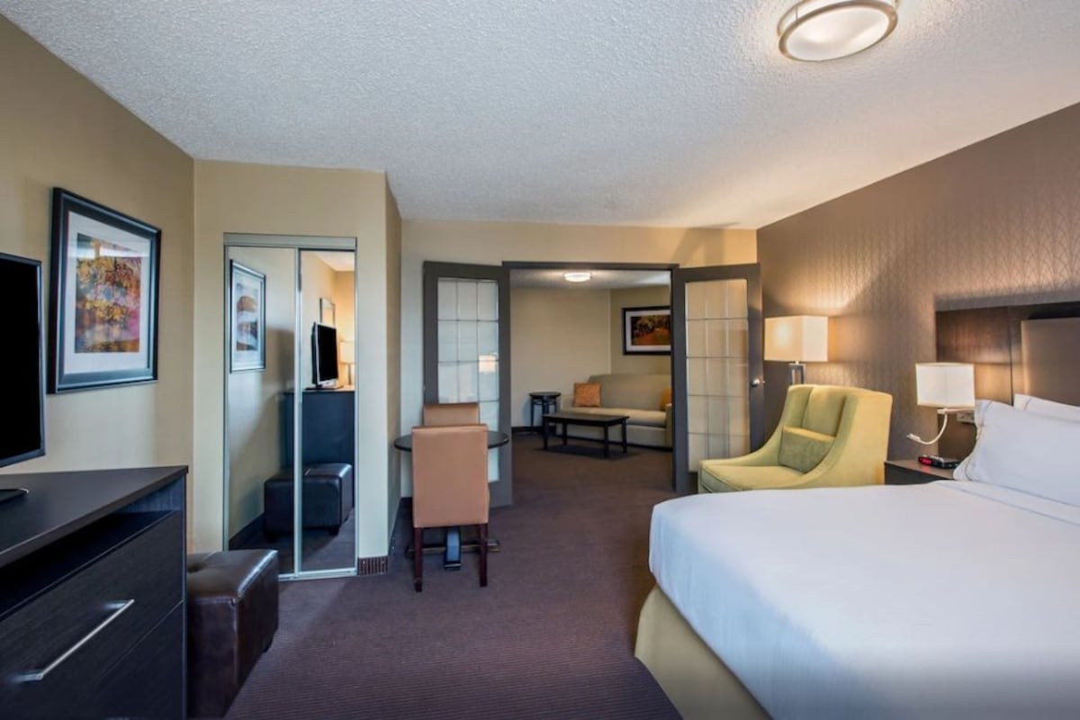 A hotel room with a bed, a desk, a chair, a television, and a painting on the wall.