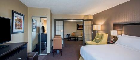 A hotel room with a bed, a desk, a chair, a television, and a painting on the wall.
