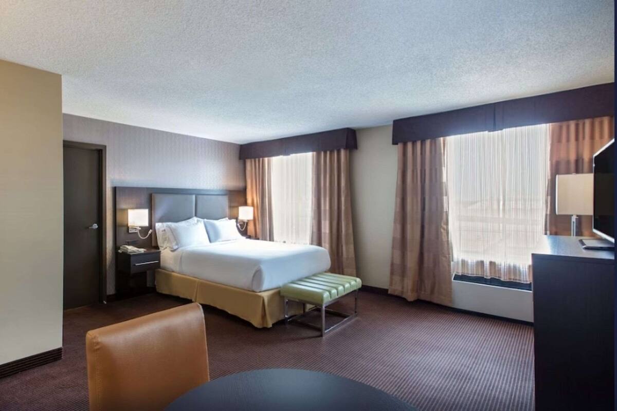 A hotel room with a bed, bedside tables, a desk, a chair, and a window with curtains.