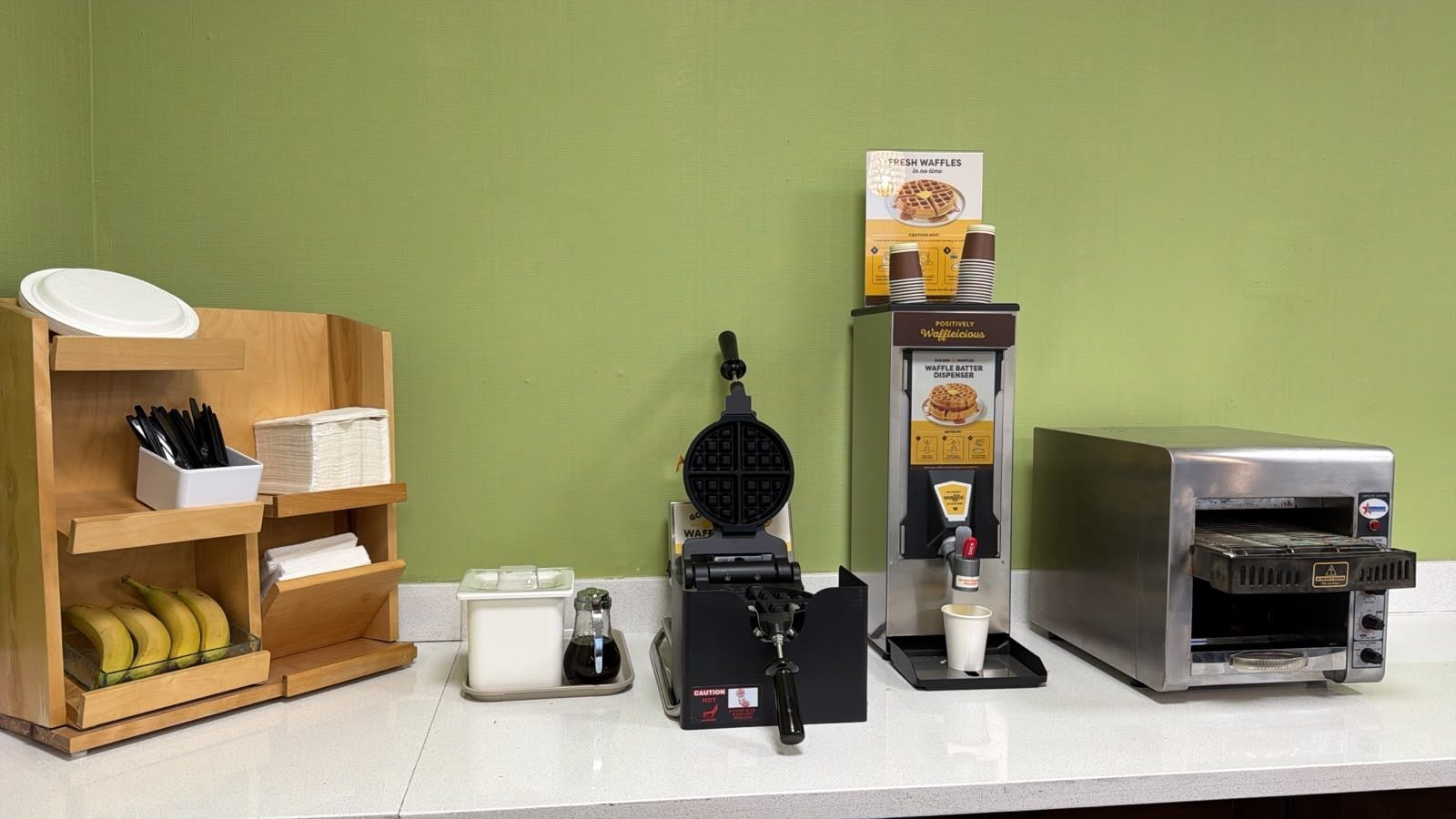 A waffle maker, a waffle batter dispenser, and a toaster oven on a counter.