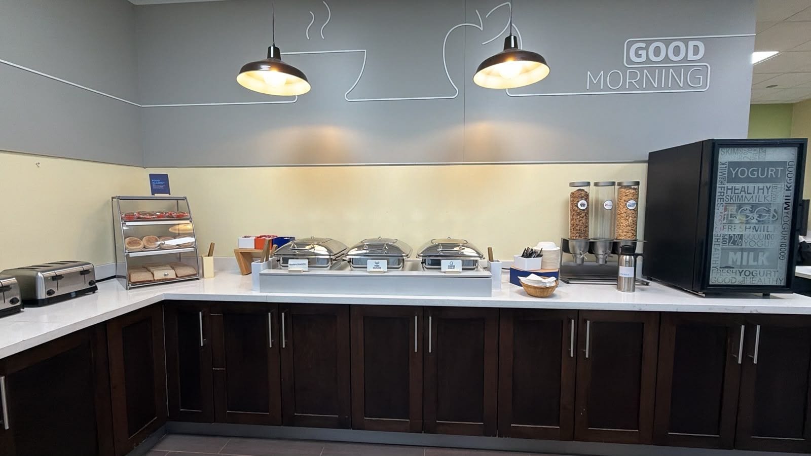A breakfast bar with a sign reading 'GOOD MORNING,' a yogurt dispenser, and a coffee machine.