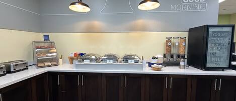 A breakfast bar with a sign reading 'GOOD MORNING,' a yogurt dispenser, and a coffee machine.