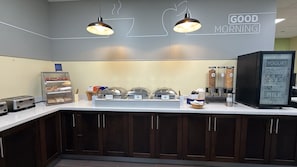 A breakfast bar with a sign reading 'GOOD MORNING,' a yogurt dispenser, and a coffee machine.