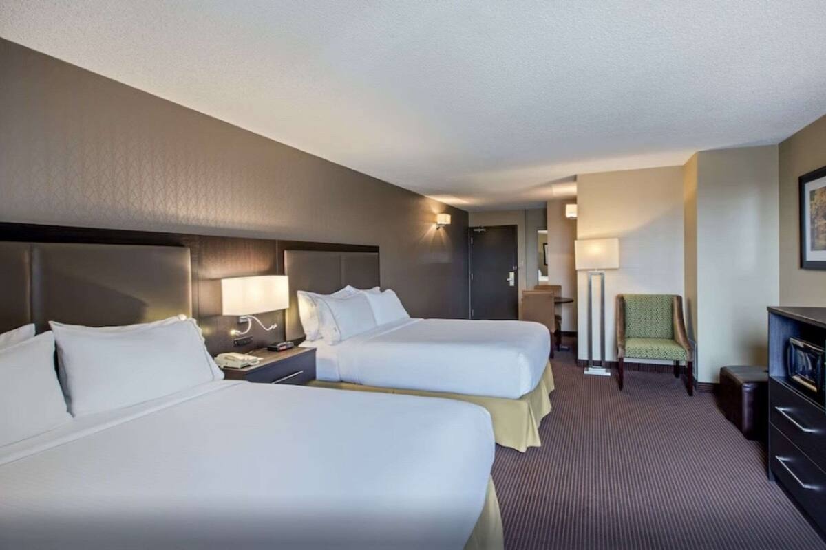 A hotel room with two beds, a desk, a chair, and a TV.