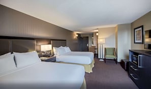 A hotel room with two beds, a desk, a chair, and a TV.