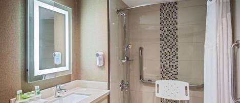 Un baño con un espejo grande, dos lavamanos, una ducha con puerta de vidrio y un perchero blanco.
