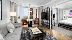 A hotel room with a sofa, two armchairs, a coffee table, a TV, a bookshelf, a bed, and a city view. - The London, a Luxury Collection Hotel, New York City (New York)