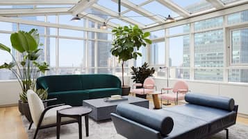 A modern living room with a green sofa, a blue sofa, and a coffee table. There are potted plants and a city view through large windows.