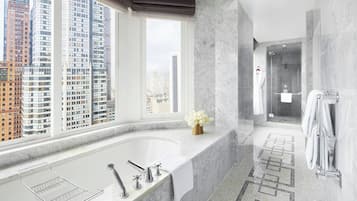 A modern bathroom with a large bathtub, a shower, and a view of tall buildings.