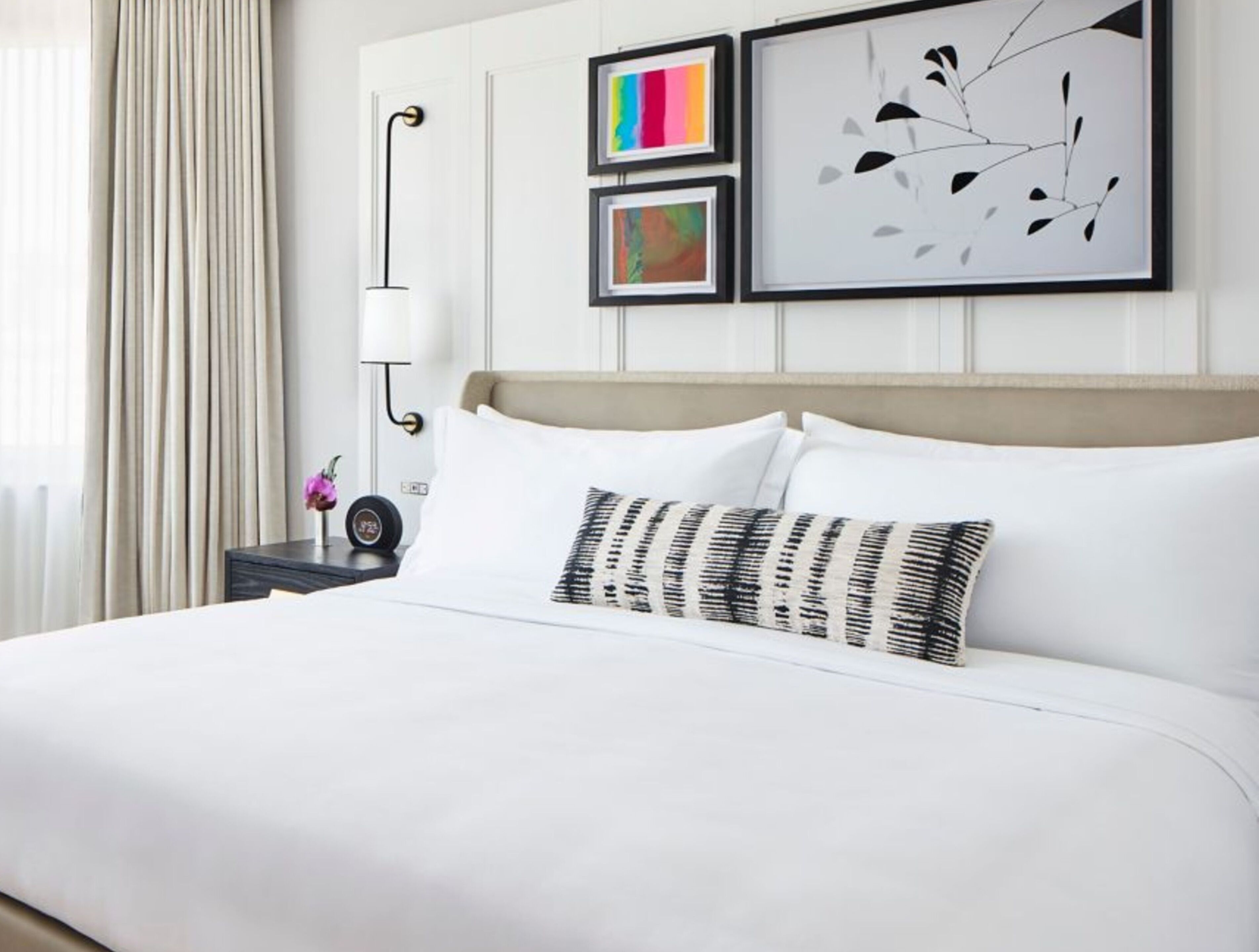 A hotel room with a large bed, a bedside table with a lamp, and three framed artworks on the wall.