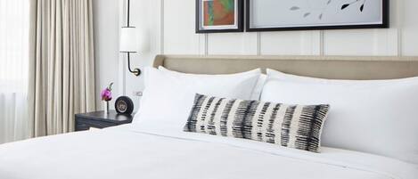 A hotel room with a large bed, a bedside table with a lamp, and three framed artworks on the wall.