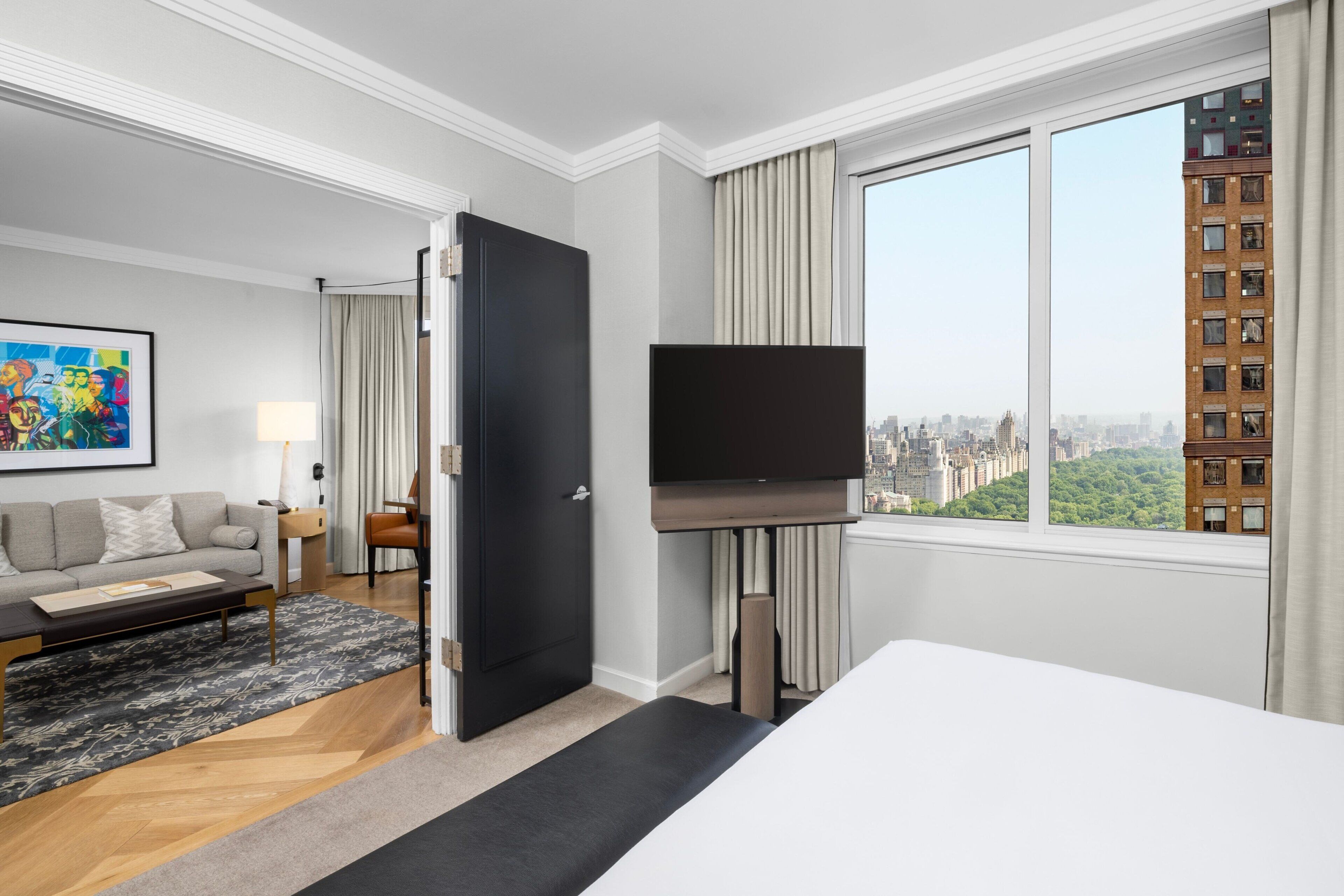 Ett hotellrum med ett stort fönster, en säng, en tv, en soffa och ett soffbord.