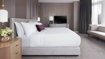 A modern hotel room with a large bed, a TV, a bedside table with a lamp, and a sofa.