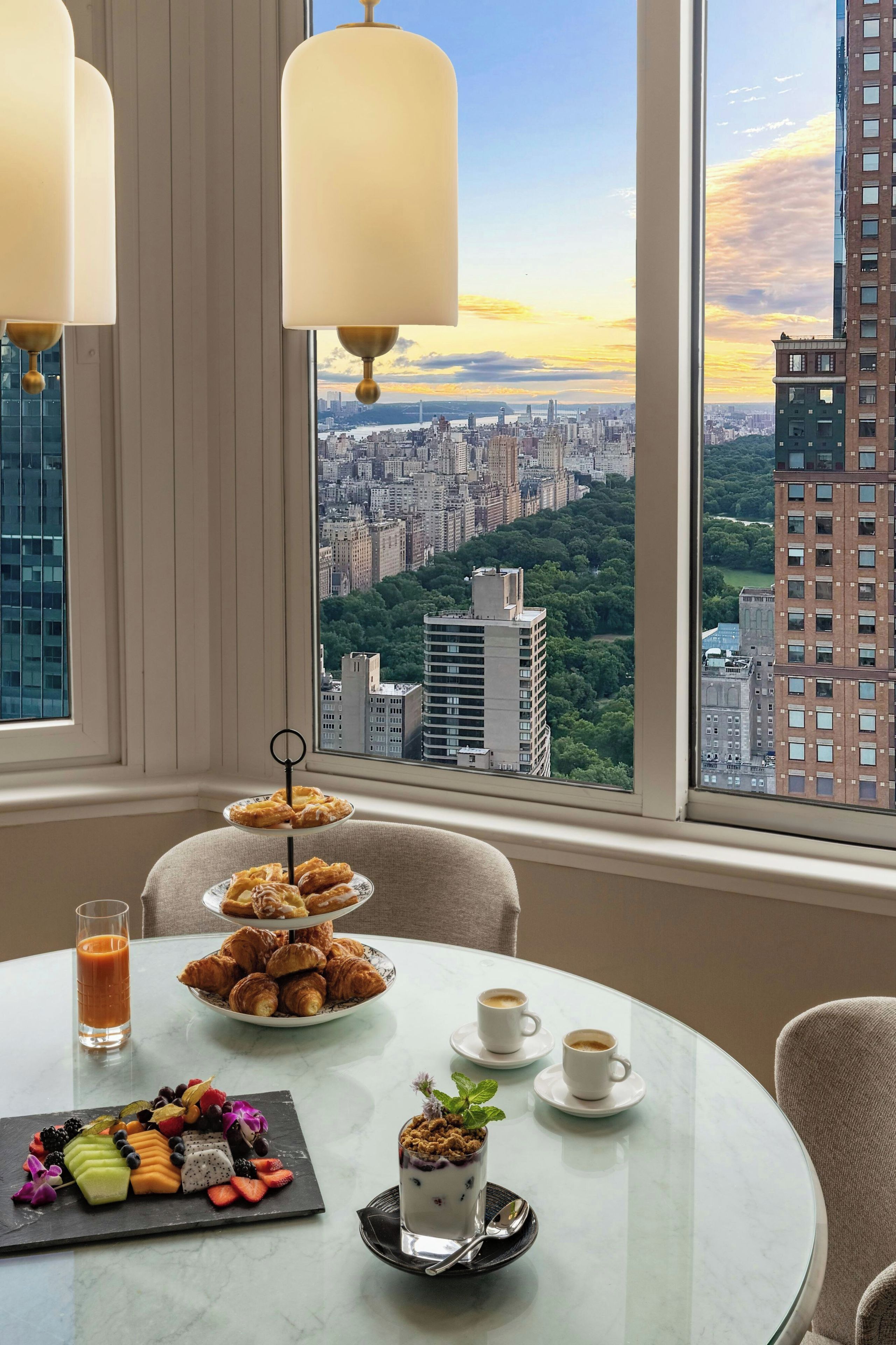 Una mesa de comedor con un plato de postres, dos tazas de café y un vaso de jugo de naranja.