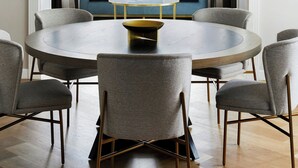 A modern dining area with a round table, grey upholstered chairs, and a gold chandelier. - The London, a Luxury Collection Hotel, New York City (New York)