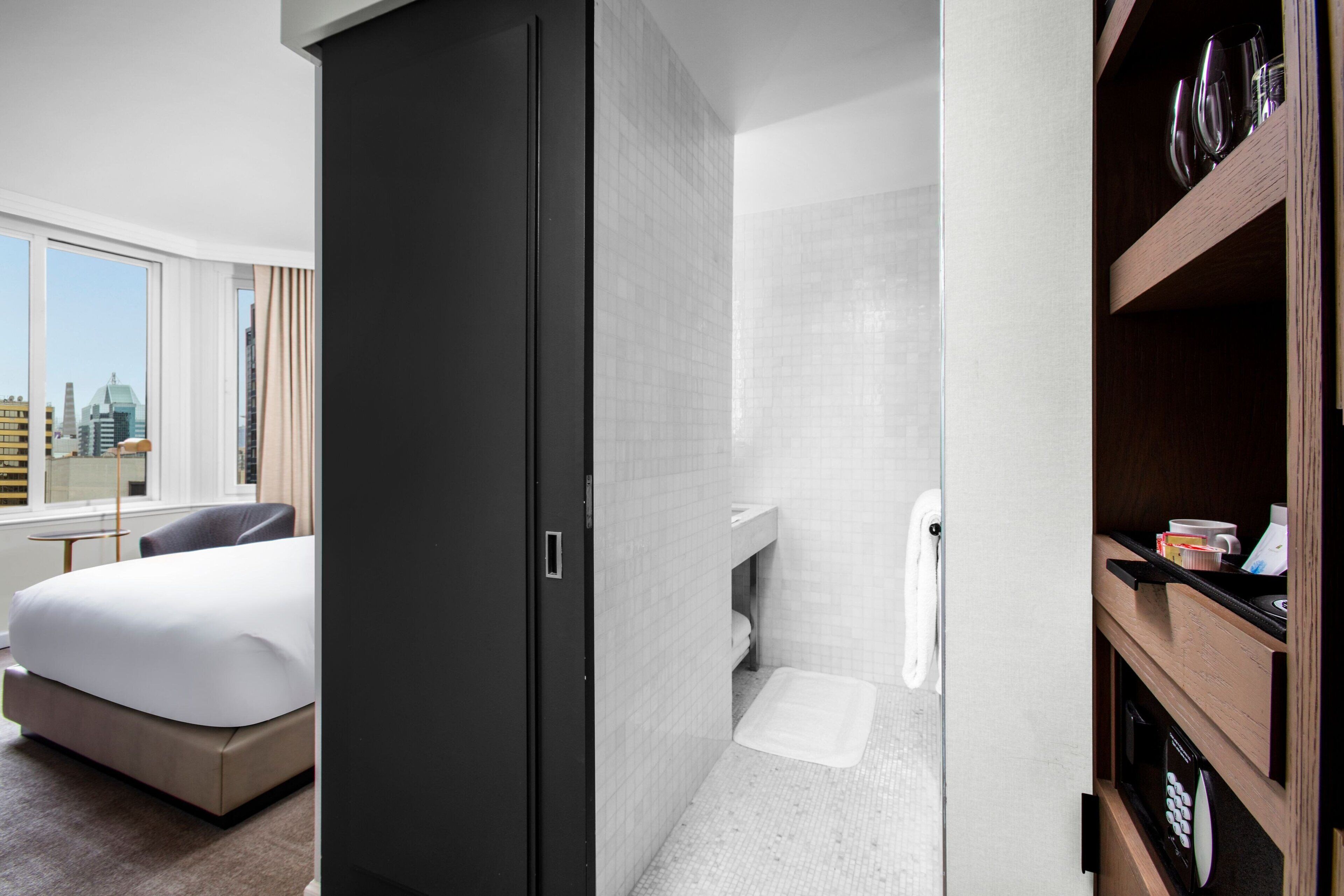Quarto de hotel com cama, guarda-roupa, casa de banho com chuveiro e vista para a cidade.