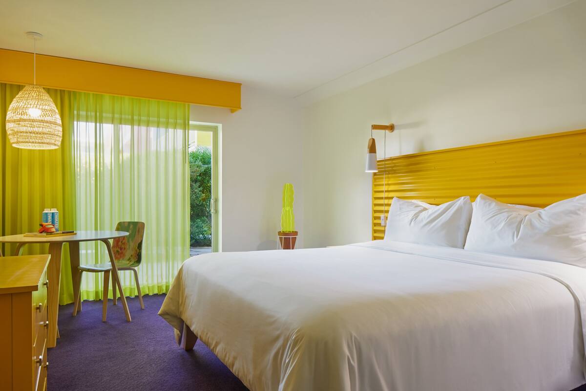 A hotel room with a large bed, a desk, a chair, and a potted plant.