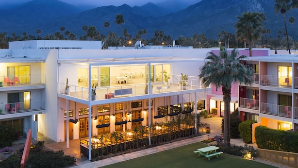 A multi-story hotel with a glass facade, outdoor seating area, and palm trees.