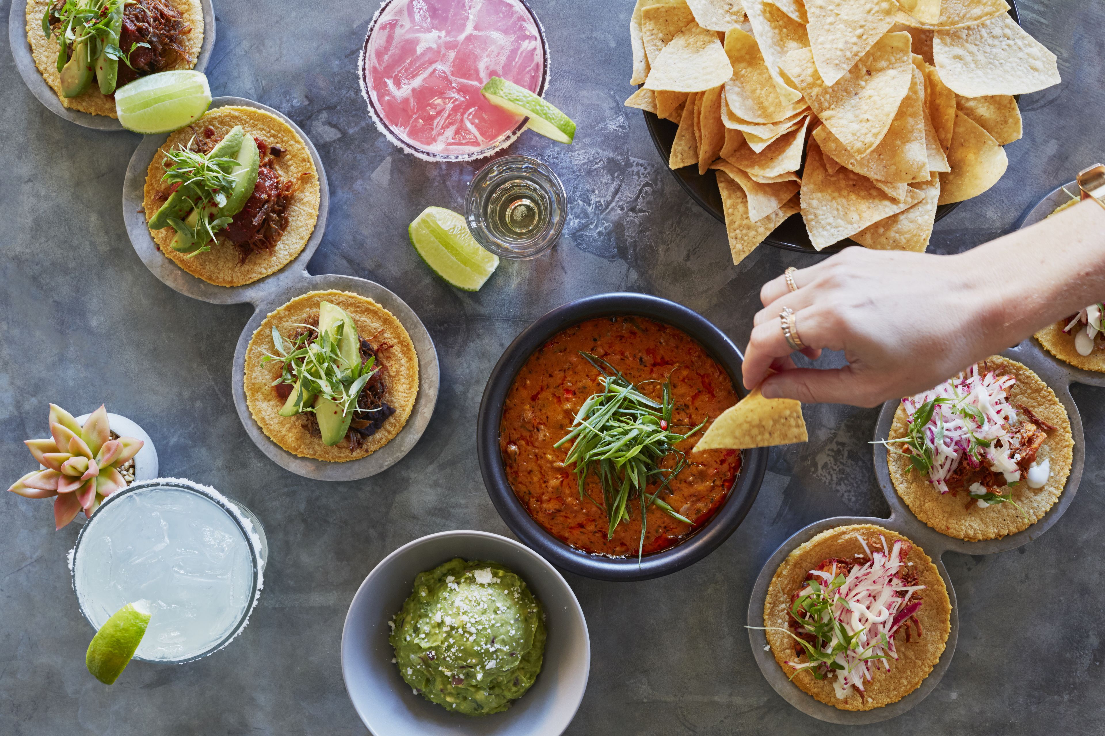 A table with various food items including tacos, chips, and drinks.