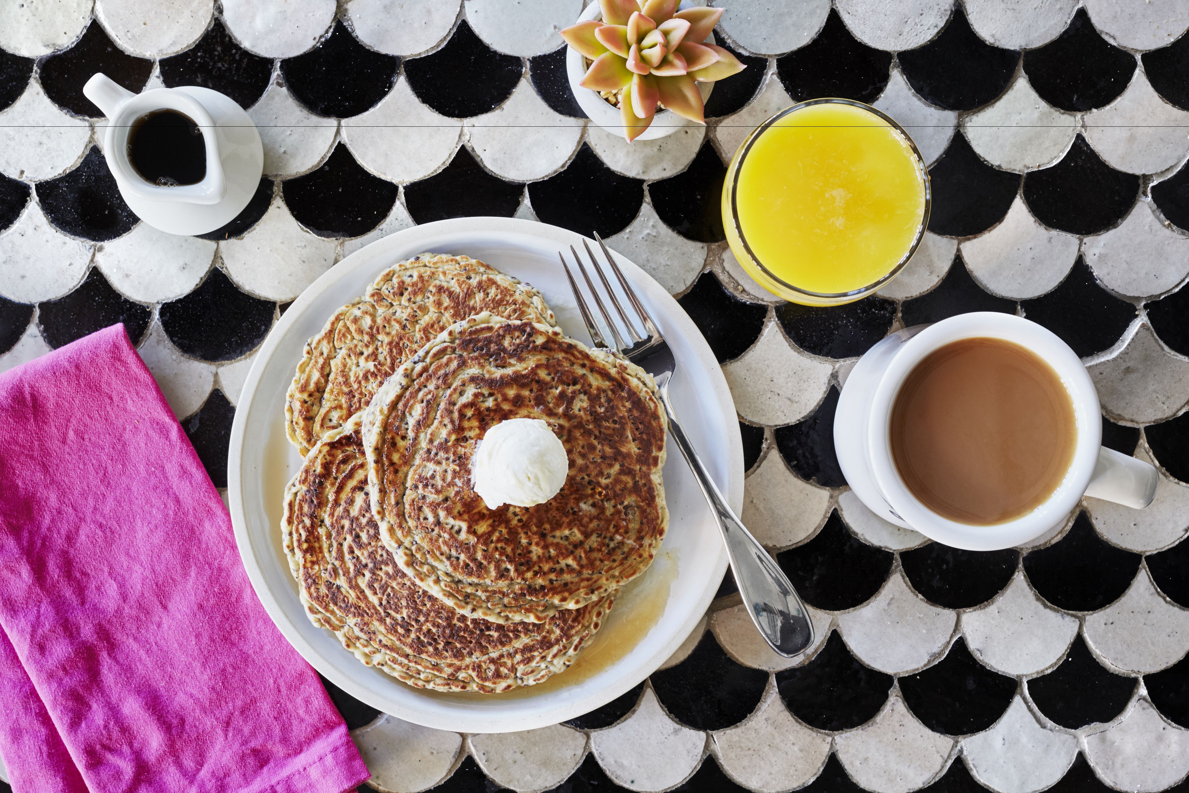 A breakfast setting with pancakes, coffee, and orange juice on a tiled table.