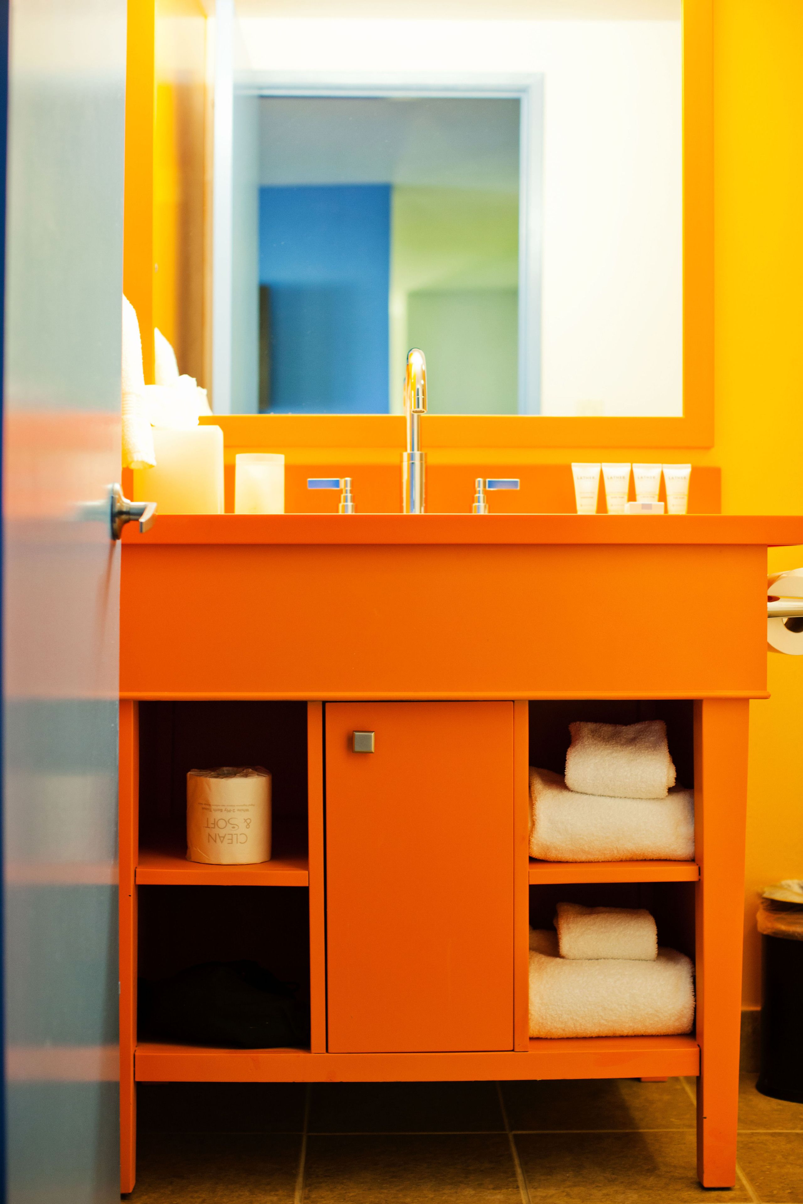 Et badeværelse med en orange vask, et spejl og en håndklædestang.