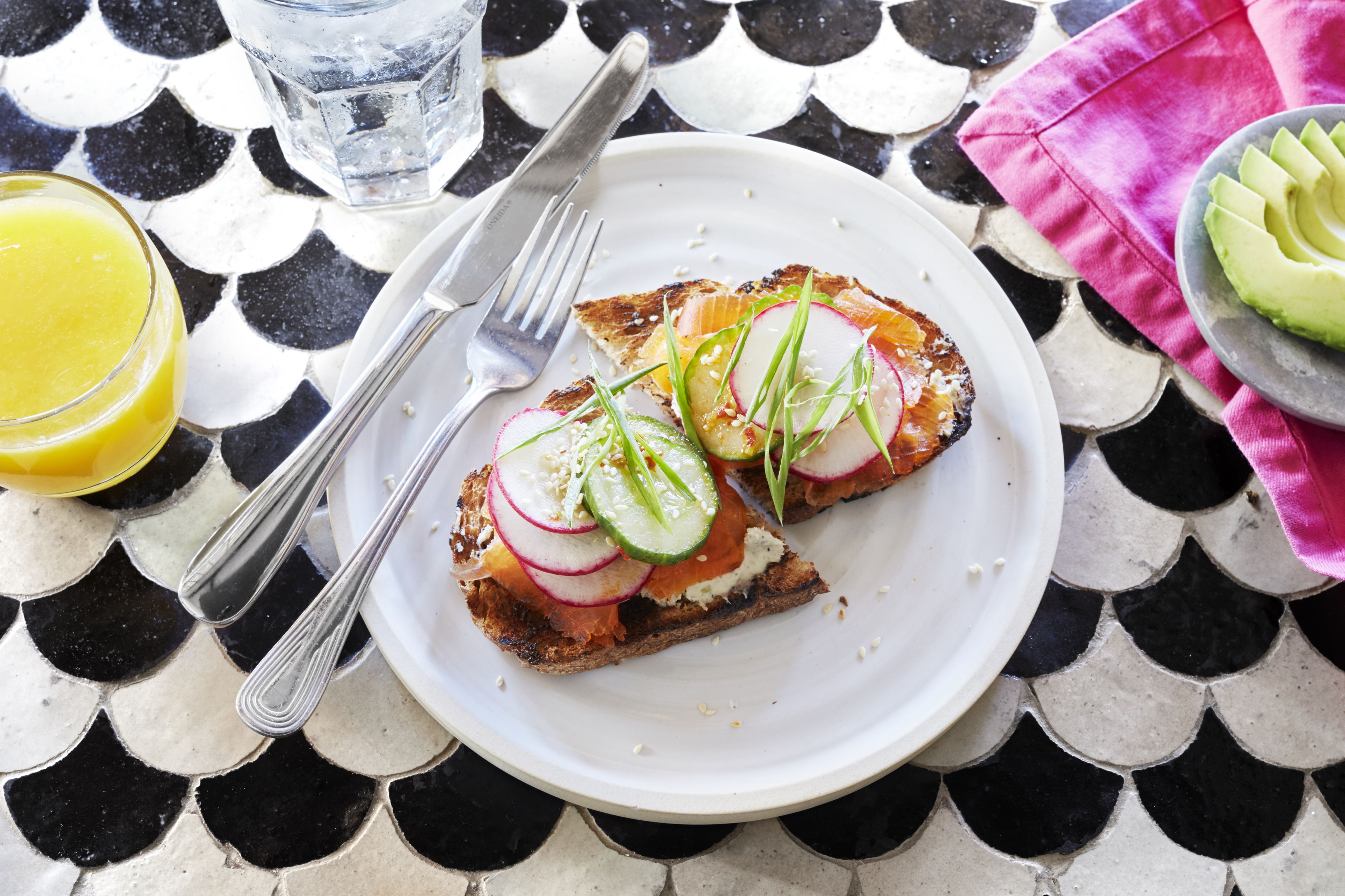 A plate with a sandwich and a glass of orange juice on a tiled table.