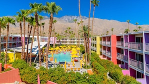 A hotel with a pool surrounded by palm trees and colorful buildings.