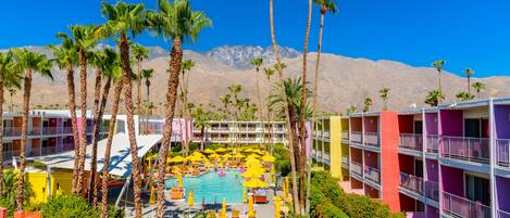 A hotel with a pool surrounded by palm trees and colorful buildings.