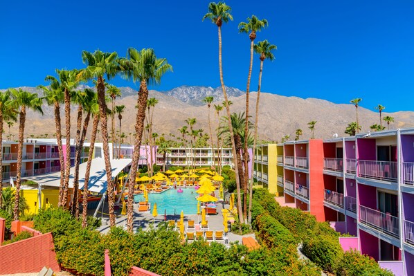 A hotel with a pool surrounded by palm trees and colorful buildings.
