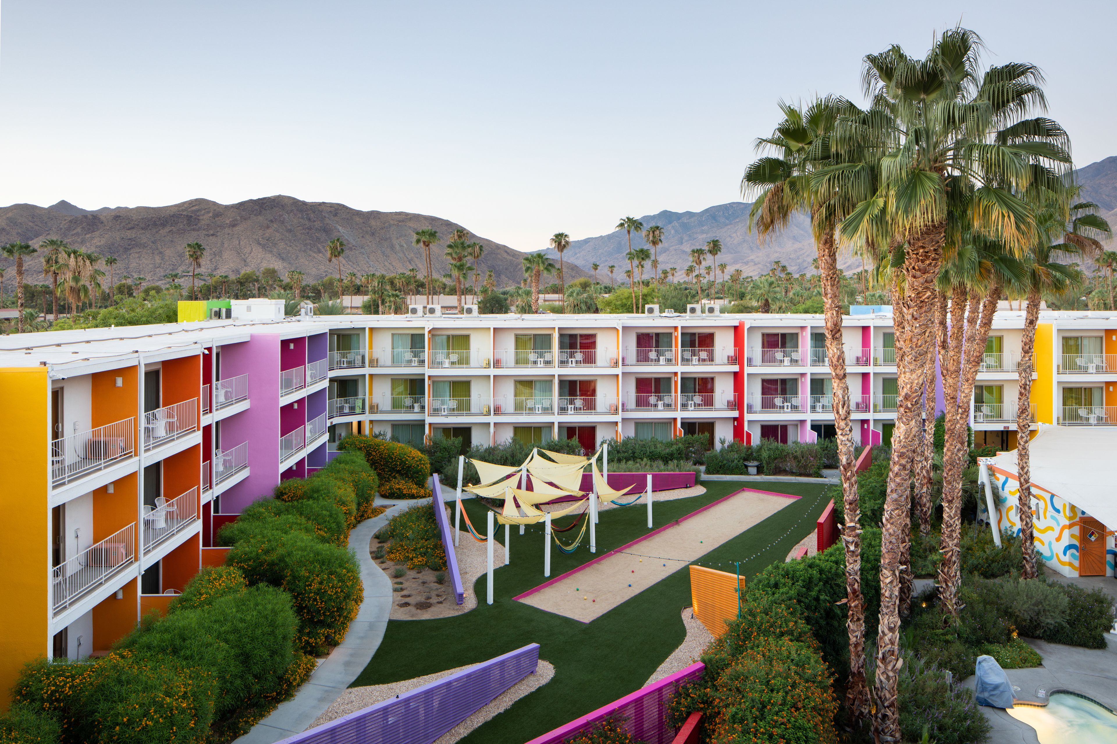 A multi-story hotel with colorful exterior walls, a courtyard with palm trees, and a pool area.