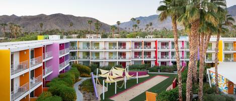 A multi-story hotel with colorful exterior walls, a courtyard with palm trees, and a pool area.