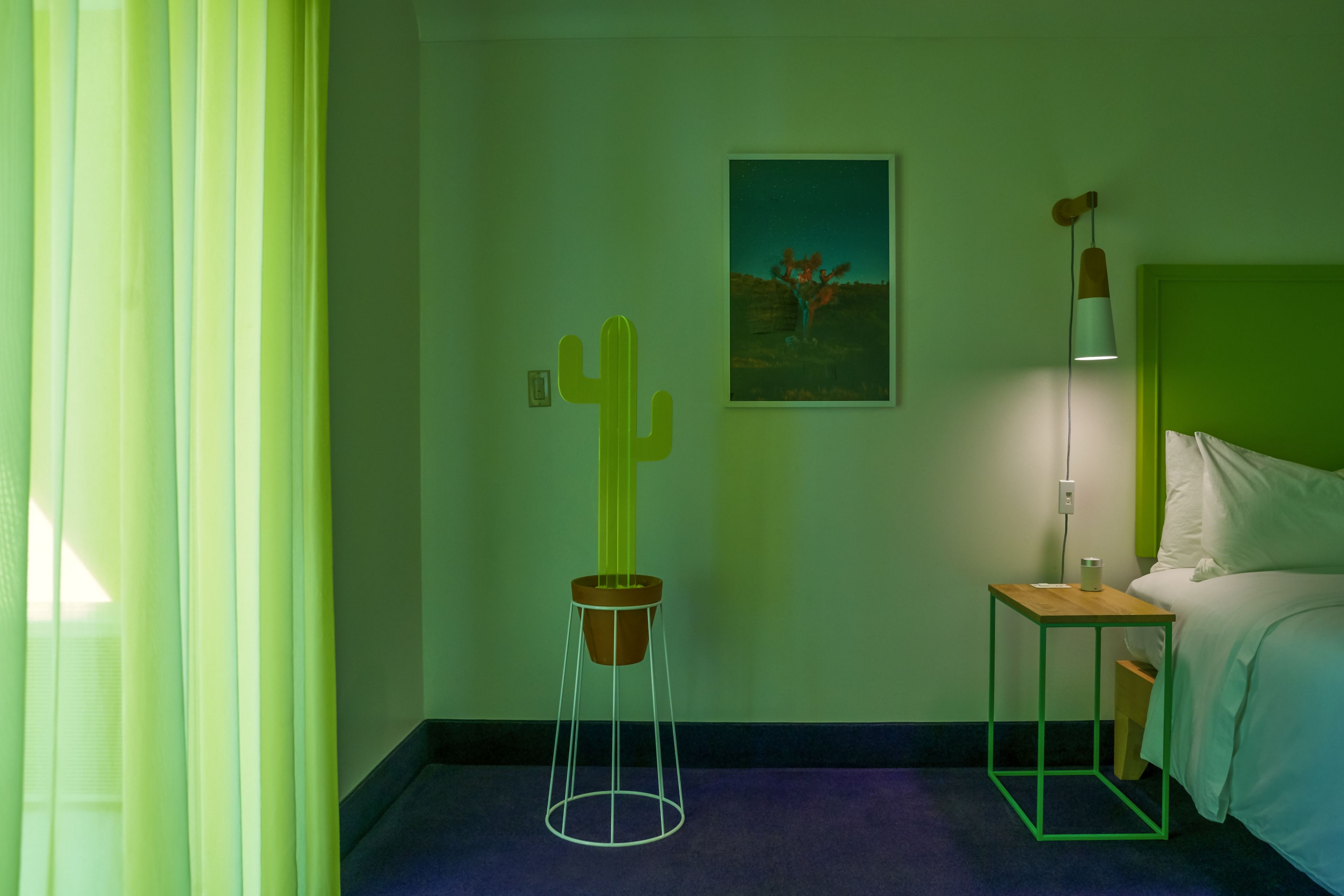 A hotel room with a bed, a nightstand, a cactus decoration, a painting, and a lamp.