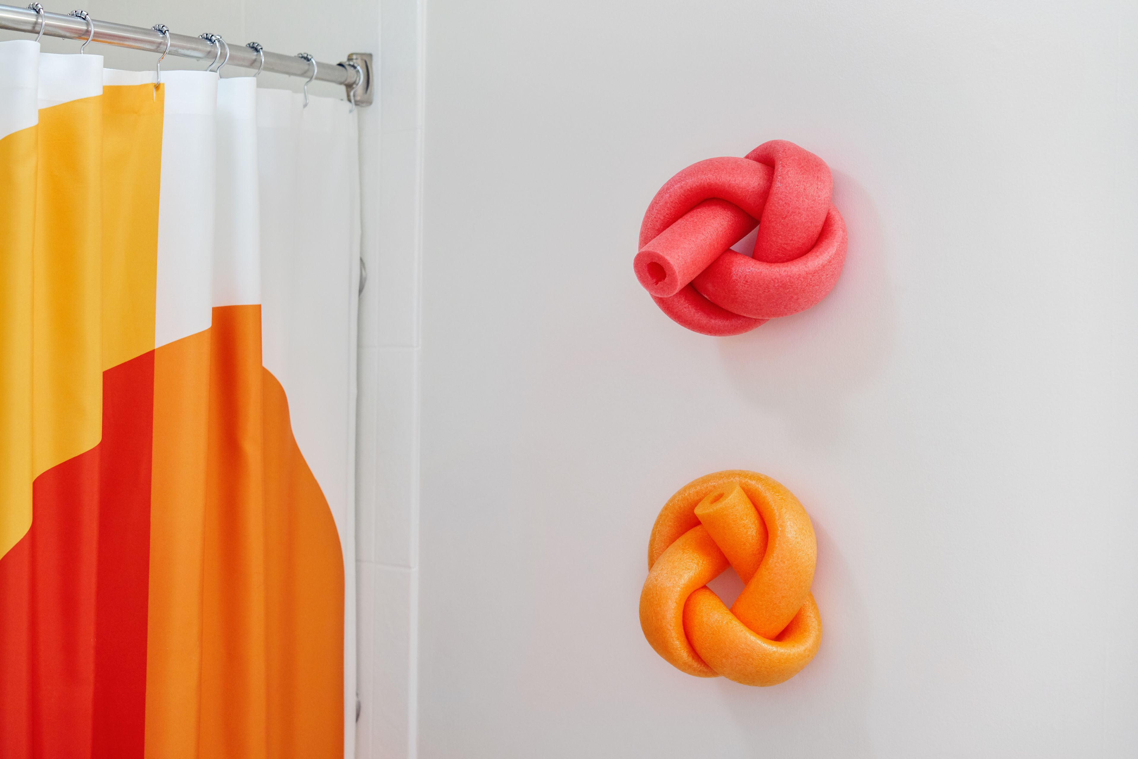 A bathroom with a shower curtain featuring a geometric pattern and two rolled-up towels on the wall.