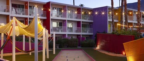 Un hotel de varios pisos con balcones, un área de juegos para niños y una mesa de arena.