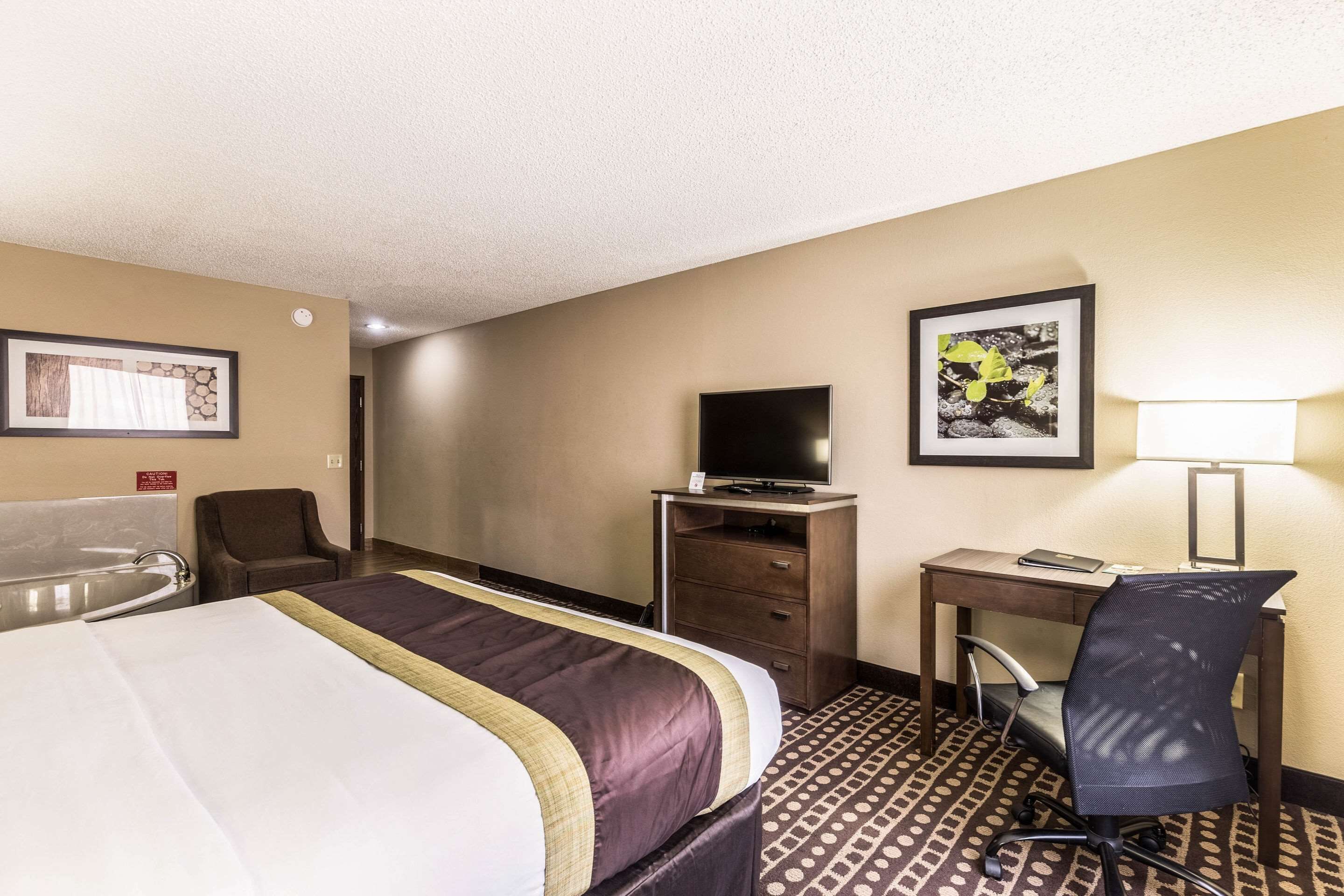 A hotel room with a large bed, a desk with a chair, a television, and a bathroom with a bathtub.