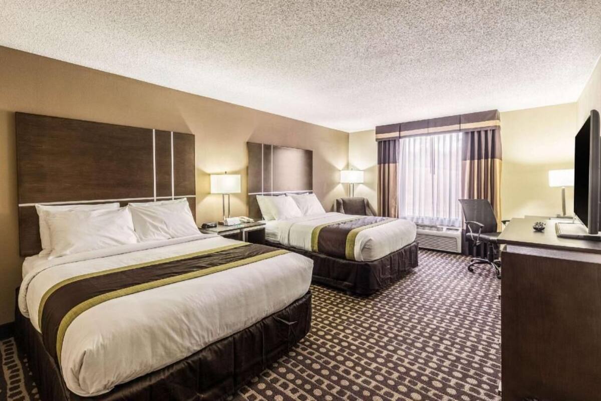 A hotel room with two beds, a desk, a TV, and a window with curtains.