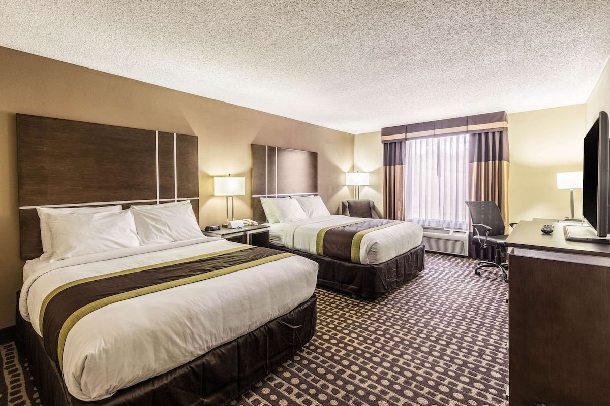 A hotel room with two beds, a desk, a chair, and a television.