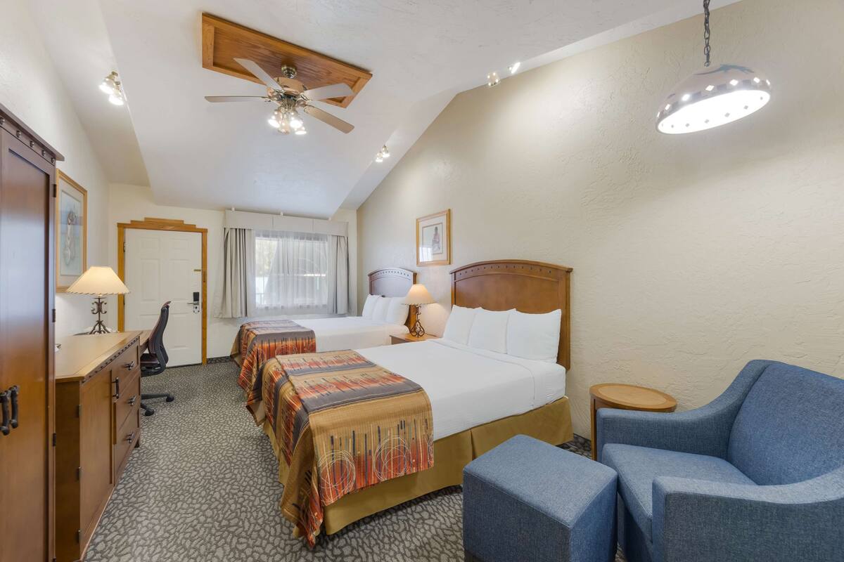 Een hotelkamer met een groot bed, twee nachtkastjes, een bureau, een stoel, een plafondventilator en een hanglamp.
