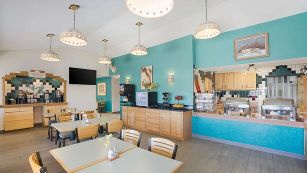 A modern cafe with wooden tables and chairs, a counter with a coffee machine, and a teal-colored wall with a painting. - Best Western Kokopelli Lodge (Clayton)