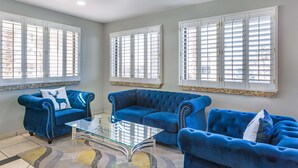 A living room with two blue sofas, a glass coffee table, and large windows with white shutters. - Best Western Sunland Park Inn (El Paso)