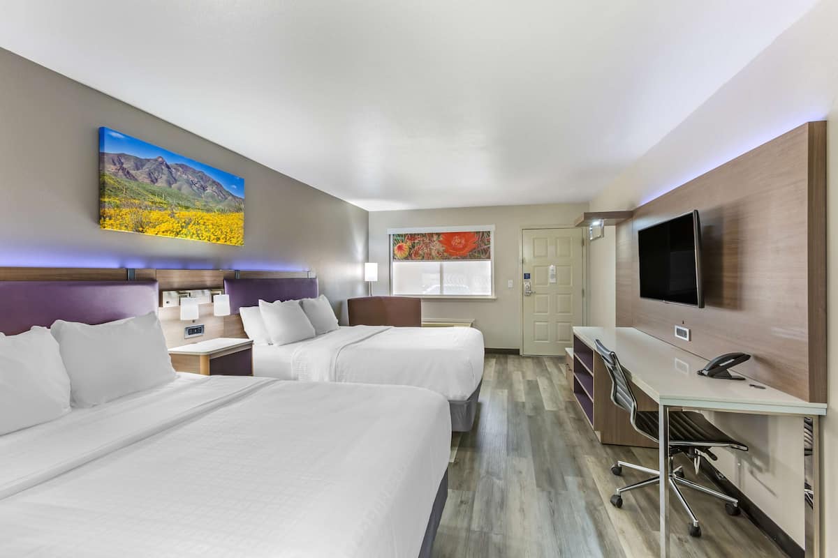 A hotel room with two beds, a desk, a TV, and artwork on the walls.