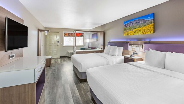 A hotel room with two beds, a TV, a desk, and a bathroom visible through an open door. - Best Western Sunland Park Inn (El Paso)
