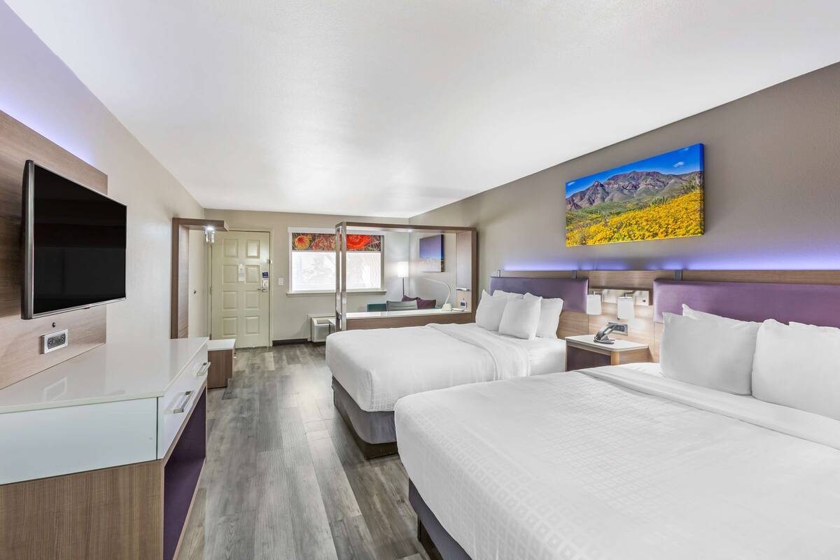 A hotel room with two beds, a TV, a desk, and a bathroom visible through an open door.