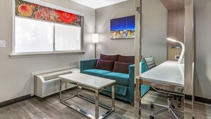 A modern room with a teal sofa, a white desk, and a large window with a view of a cityscape. - Best Western Sunland Park Inn (El Paso)