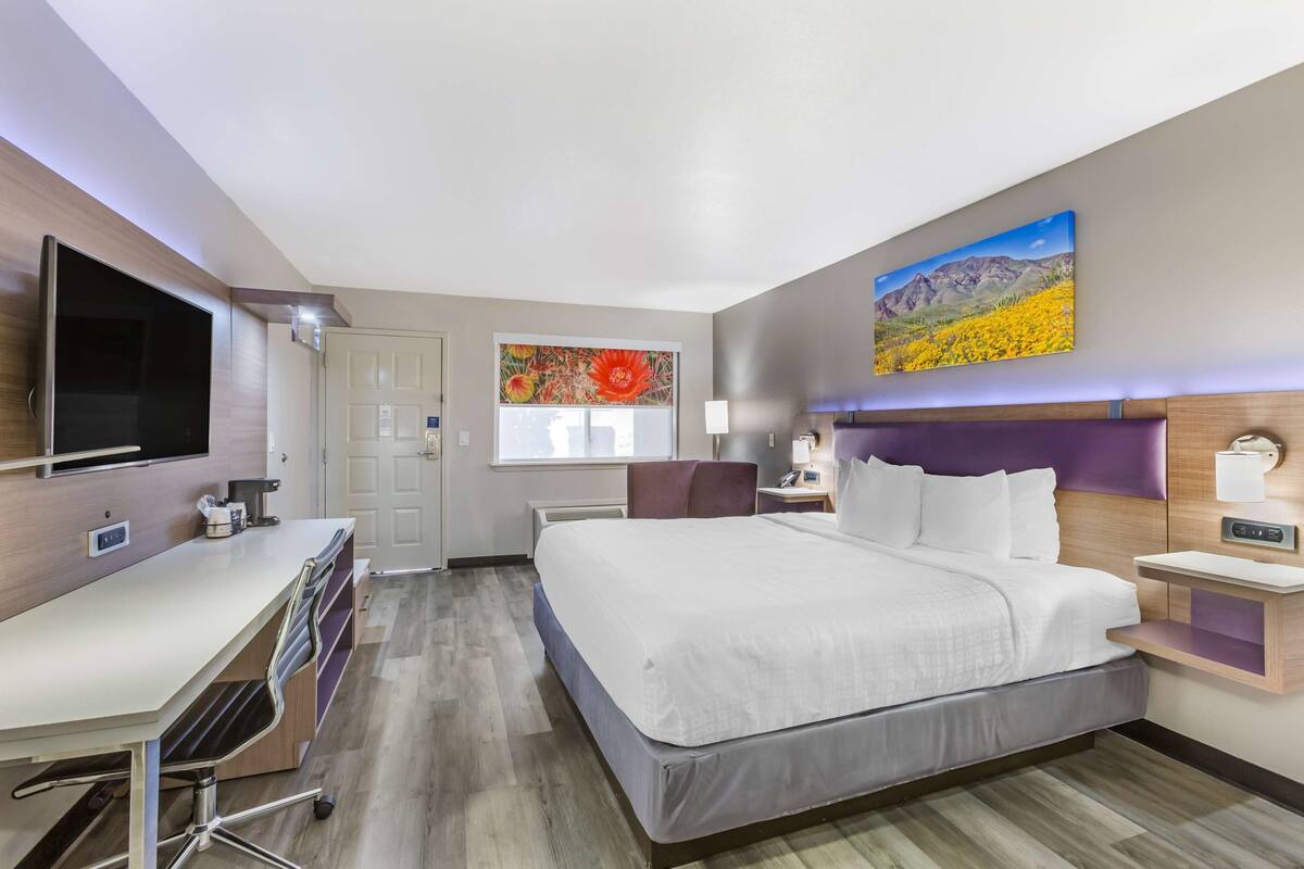 A hotel room with a large bed, a desk with a computer, a flat-screen TV, and artwork on the walls.