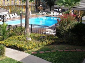 A swimming pool surrounded by lounge chairs and greenery, with a building in the background. - Americas Best Value Inn Laredo (Laredo)