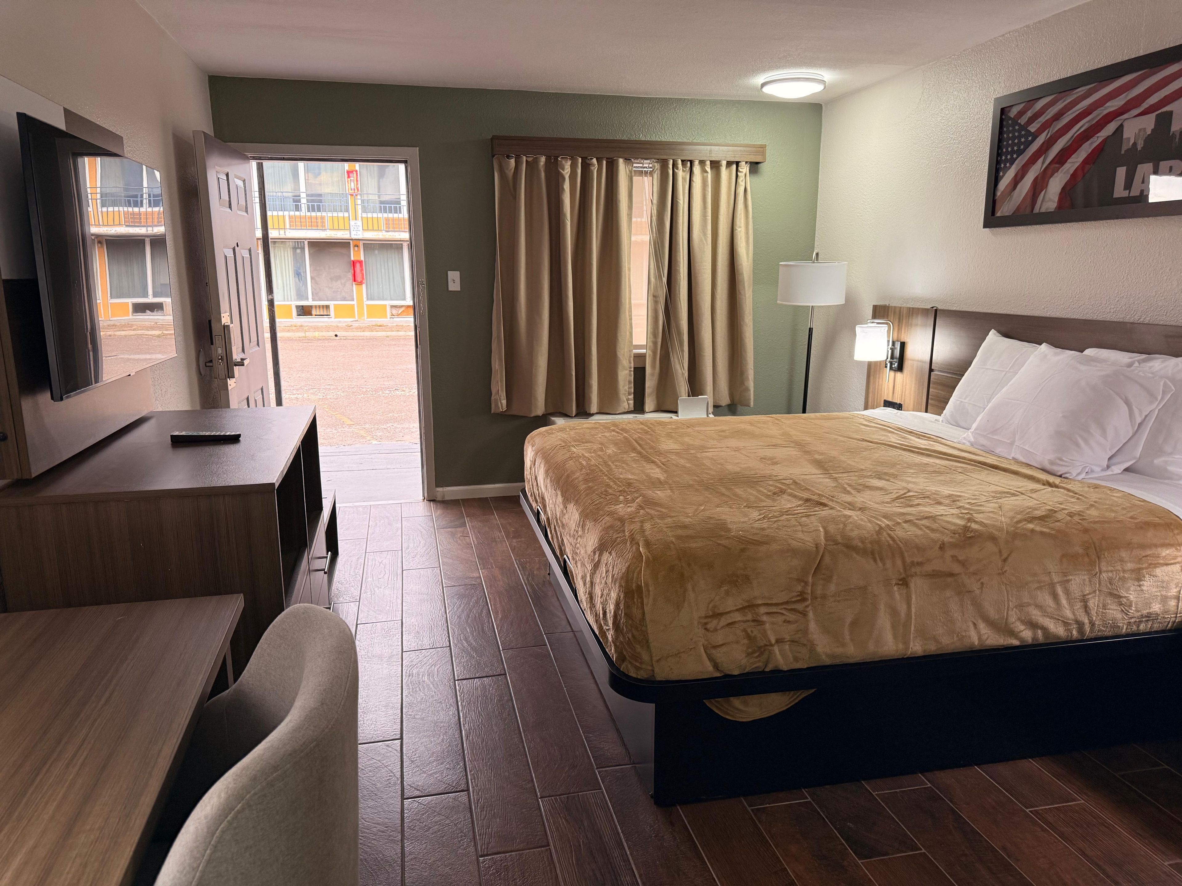 Una camera d'albergo con un letto, una scrivania, una sedia, un televisore e una finestra con tende.